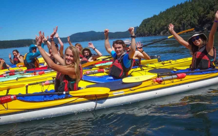 a group of kayakers raise their arms in the air on a sea kayaking trip with outward bound